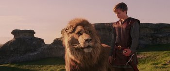 Movie still from “The Chronicles of Narnia: The Lion, the Witch and the Wardrobe” (2005), directed by Andrew Adamson – A man standing next to a lion in a field; Medium shot, Low angle