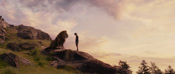 Movie still from “The Chronicles of Narnia: The Lion, the Witch and the Wardrobe” (2005), directed by Andrew Adamson – A man standing on top of a hill next to a lion; Wide shot, Low angle