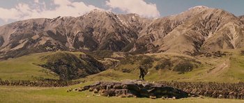Movie still from “The Chronicles of Narnia: The Lion, the Witch and the Wardrobe” (2005), directed by Andrew Adamson – A person standing on a rock in a field with mountains in the background; Extreme Wide shot, Low angle