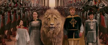 Movie still from “The Chronicles of Narnia: The Lion, the Witch and the Wardrobe” (2005), directed by Andrew Adamson – A couple of people standing in front of a lion; Wide shot, High angle