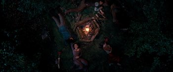 Movie still from “The Chronicles of Narnia: Prince Caspian” (2008), directed by Andrew Adamson – A group of people laying in the grass next to a fire pit; Wide shot, Overhead angle