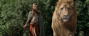 Movie still from “The Chronicles of Narnia: Prince Caspian” (2008), directed by Andrew Adamson – A woman standing next to a lion in a wooded area; Medium shot, Low angle