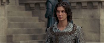Movie still from “The Chronicles of Narnia: Prince Caspian” (2008), directed by Andrew Adamson – A young man in renaissance garb stands in front of a statue; Medium shot, Over the shoulder angle