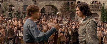 Movie still from “The Chronicles of Narnia: Prince Caspian” (2008), directed by Andrew Adamson – A man holding a sword in front of a crowd of onlookers; Wide shot, Over the shoulder angle