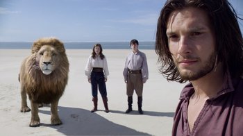 Movie still from “The Chronicles of Narnia: The Voyage of the Dawn Treader” (2010), directed by Michael Apted – Two men and a woman standing in front of a lion on the beach; Medium shot, Low angle