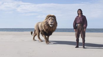 Movie still from “The Chronicles of Narnia: The Voyage of the Dawn Treader” (2010), directed by Michael Apted – A man standing next to a lion on the beach; Wide shot, Low angle
