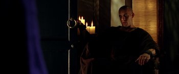 Movie still from “The Chronicles of Riddick” (2004), directed by David Twohy – A man sitting in front of a door holding a candle; Medium shot, Low angle