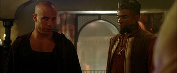 Movie still from “The Chronicles of Riddick” (2004), directed by David Twohy – Two men standing next to each other in front of a building; Medium shot, Over the shoulder angle