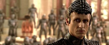 Movie still from “The Chronicles of Riddick” (2004), directed by David Twohy – A person wearing a helmet with a bunch of people in the background; Close Up shot, Over the shoulder angle