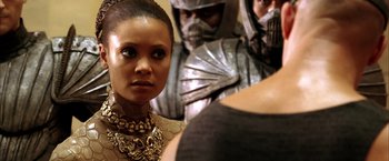 Movie still from “The Chronicles of Riddick” (2004), directed by David Twohy – A woman standing in front of two men in armor; Close Up shot, Over the shoulder angle
