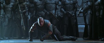 Movie still from “The Chronicles of Riddick” (2004), directed by David Twohy – A man is laying on the ground in front of a bunch of statues; Wide shot, Low angle