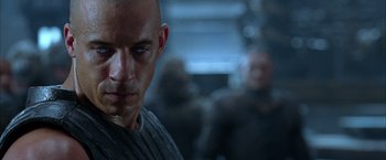 Movie still from “The Chronicles of Riddick” (2004), directed by David Twohy – A man with a shaved head and a blue eye; Close Up shot, Over the shoulder angle