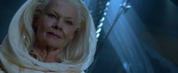 Movie still from “The Chronicles of Riddick” (2004), directed by David Twohy – An older woman with blonde hair wearing a white robe; Close Up shot, Low angle