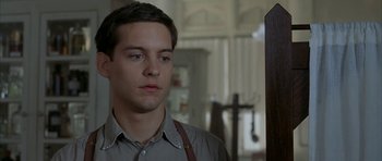 Movie still from “The Cider House Rules” (1999), directed by Lasse Hallström – A man in a gray shirt and brown suspenders looks at the camera; Close Up shot, Low angle