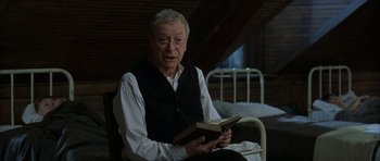 Movie still from “The Cider House Rules” (1999), directed by Lasse Hallström – An older man sitting in a chair holding an open book; Medium shot, Low angle