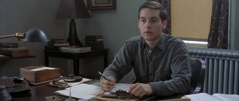 Movie still from “The Cider House Rules” (1999), directed by Lasse Hallström – A man sitting at a table writing on a piece of paper; Medium shot, High angle
