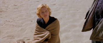 Movie still from “The Cider House Rules” (1999), directed by Lasse Hallström – A woman wrapped in a blanket sitting on the beach; Medium shot, High angle