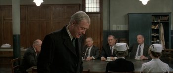 Movie still from “The Cider House Rules” (1999), directed by Lasse Hallström – An older man standing in front of a group of people; Medium shot, Over the shoulder angle