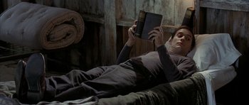 Movie still from “The Cider House Rules” (1999), directed by Lasse Hallström – A man laying on a bed reading a book; Medium shot, High angle