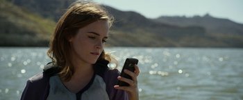 Movie still from “The Circle” (2017), directed by James Ponsoldt – A woman looking at her cell phone while standing in front of a body of water; Close Up shot, Low angle
