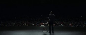 Movie still from “The Circle” (2017), directed by James Ponsoldt – A man standing on a stage in front of an audience; Wide shot, High angle