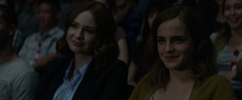Movie still from “The Circle” (2017), directed by James Ponsoldt – Two women sitting in front of each other in front of a group of people; Close Up shot, Over the shoulder angle