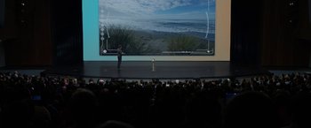 Movie still from “The Circle” (2017), directed by James Ponsoldt – A man standing on a stage in front of a large screen; Extreme Wide shot, High angle