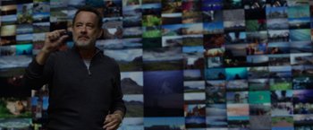 Movie still from “The Circle” (2017), directed by James Ponsoldt – A man standing in front of a bunch of pictures; Medium shot, High angle