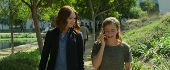 Movie still from “The Circle” (2017), directed by James Ponsoldt – Two young women walking on a path talking on a cell phone; Medium shot, Over the shoulder angle