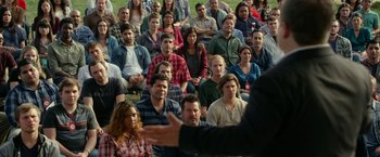 Movie still from “The Circle” (2017), directed by James Ponsoldt – A group of people sitting in a field with a man speaking; Wide shot, Over the shoulder angle