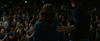 Movie still from “The Circle” (2017), directed by James Ponsoldt – A woman in a blue dress is hugging a man in front of a crowd of onlookers; Medium shot, Over the shoulder angle