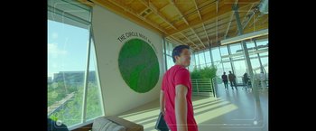 Movie still from “The Circle” (2017), directed by James Ponsoldt – A man in a red shirt is standing in front of a wall with a globe on it; Extreme Wide shot, High angle