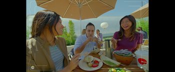 Movie still from “The Circle” (2017), directed by James Ponsoldt – A group of people sitting at a table eating food under an umbrella; Medium shot, High angle