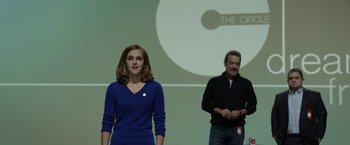 Movie still from “The Circle” (2017), directed by James Ponsoldt – A woman standing next to a man in front of a projection screen; Medium shot, Over the shoulder angle
