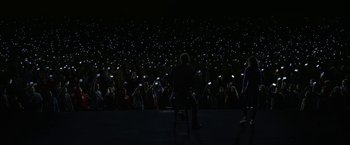 Movie still from “The Circle” (2017), directed by James Ponsoldt – A group of people sitting in front of an audience at night with cell phones; Extreme Wide shot, High angle