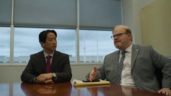 Movie still from “Full Circle” (2023), directed by Steven Soderbergh – Two men sitting at a table in front of a window; Medium shot, Over the shoulder angle