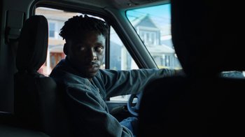Movie still from “Full Circle” (2023), directed by Steven Soderbergh – A man sitting in the driver's seat of a car; Close Up shot, Low angle