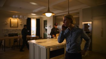Movie still from “Full Circle” (2023), directed by Steven Soderbergh – A woman talking on a phone while standing in front of a kitchen counter; Medium shot, Low angle