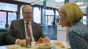 Movie still from “Full Circle” (2023), directed by Steven Soderbergh – A man and a woman sitting at a table with a plate of pizza; Medium shot, Over the shoulder angle