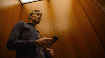 Movie still from “Full Circle” (2023), directed by Steven Soderbergh – A man holding a cell phone while standing next to a door; Medium shot, Low angle