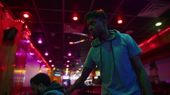 Movie still from “Full Circle” (2023), directed by Steven Soderbergh – A young man standing in front of a ceiling with lights on; Medium shot, Over the shoulder angle