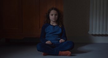 Movie still from “Petite Maman” (2021), directed by Céline Sciamma – A girl sitting on the ground holding a remote control; Medium shot, High angle