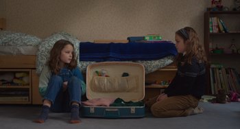 Movie still from “Petite Maman” (2021), directed by Céline Sciamma – Two young girls sitting on the floor next to an open suitcase; Medium shot, High angle