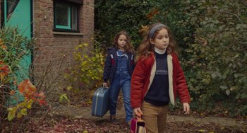 Movie still from “Petite Maman” (2021), directed by Céline Sciamma – Two young girls walking down a path holding suitcases; Medium shot, High angle