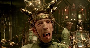 Movie still from “The City of Lost Children” (1995), directed by Jean-Pierre Jeunet – A man wearing a green shirt and a crown of beer bottles on top of his head; Close Up shot, Low angle