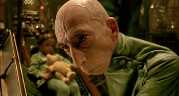 Movie still from “The City of Lost Children” (1995), directed by Jean-Pierre Jeunet – A man with a bald head is holding a teddy bear; Close Up shot, Low angle