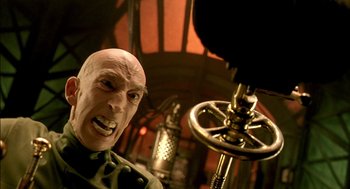 Movie still from “The City of Lost Children” (1995), directed by Jean-Pierre Jeunet – A man with a bald head is looking into a microphone; Close Up shot, Low angle