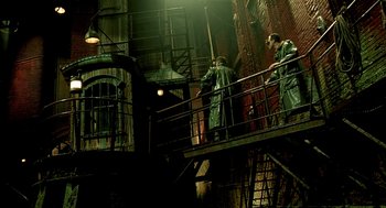 Movie still from “The City of Lost Children” (1995), directed by Jean-Pierre Jeunet – A group of people standing on a metal railing near a building; Wide shot, High angle