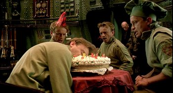 Movie still from “The City of Lost Children” (1995), directed by Jean-Pierre Jeunet – A group of men standing around a cake with lit candles on it; Medium shot, Overhead angle