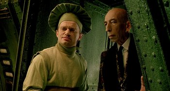 Movie still from “The City of Lost Children” (1995), directed by Jean-Pierre Jeunet – A man in a chef's hat and a man in a suit and tie standing next to each other; Medium shot, Low angle